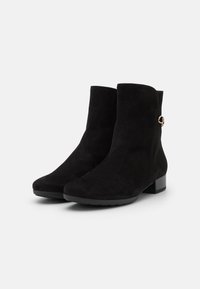 Svarta mockaskor med rund tå, låg blockklack och en dekorativ guldfinish på sidan. Slät textur och stilren design.