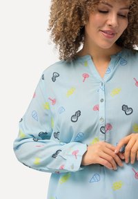 Camicia button-up azzurro chiaro con motivi giocosi a tema caramelle in rosso, giallo e nero, dotata di maniche lunghe e una vestibilità leggermente rilassata.
