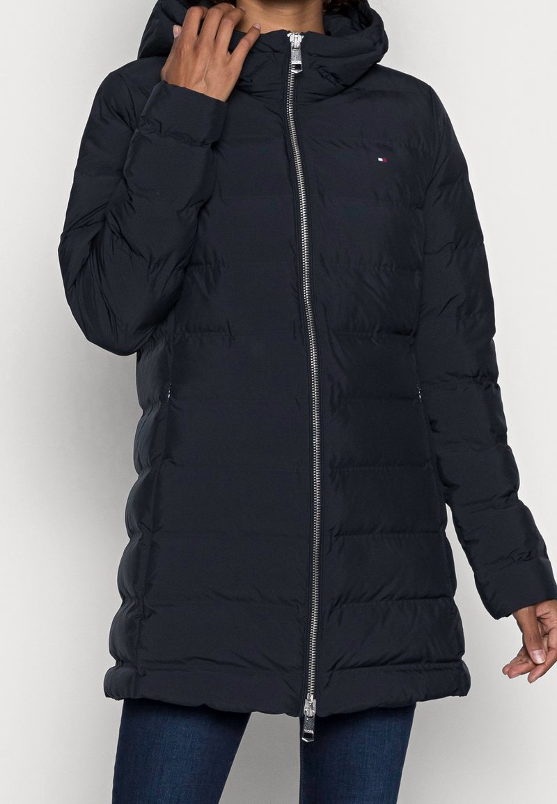 Tumma pusakka, jossa on vetskari edessä, huppu ja tikattu kuvio. Varustettu pienellä logolla ja sivutaskuilla. Valmistettu kevyestä materiaalista.