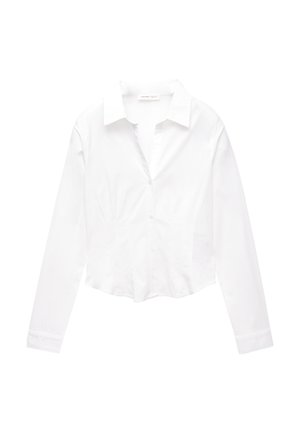 Chemise blanche à manches longues, ajustée, avec col, longueur légèrement raccourcie et texture en coton lisse. Sans motifs ni accents.