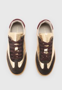 Sneakers con pelle metallizzata dorata e suede marrone scuro. Punta arrotondata, lacci bordeaux e suola in gomma con motivi testurizzati.