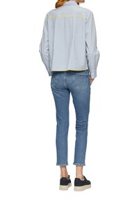 Gestreiftes blaues Hemd mit einem cropped Design, das am Saum eine gelbe Akzentuierung aufweist. Kombiniert mit hellblauen slim-fit Jeans und schwarzen Plateausneakern.