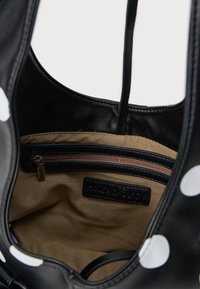Zwarte tas met een beige binnenvoering, voorzien van een ritszak, leren accenten en een stippenpatroon aan de buitenkant.