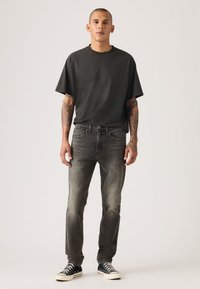 Μαύρο μπλουζάκι, γκρι τζιν και μαύρα αθλητικά παπούτσια. Το ύφασμα είναι απαλό με άνετη εφαρμογή. Τα τζιν έχουν ξεθωριασμένη όψη και λεπτομέρειες διακριτικής ραφής.