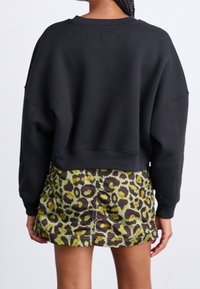Sweatshirt noir court avec manches larges, associé à une mini-jupe à imprimé léopard vert et marron avec des détails froncés.