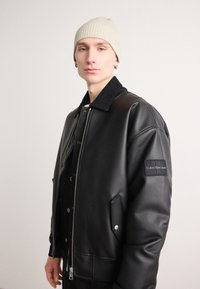Juodas odinis bomber tipo švarkas su šriuose užtrauktuku ir šoninėmis kišenėmis. Pasižymi užtrauktuko priekyje ir Calvin Klein Jeans logotipo ženkleliu ant rankovės.