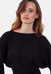 Schwarzer Pullover mit weiter Boot-Ausschnitt, locker sitzenden Ärmeln und weichem, strukturiertem Stoff. Einfaches Design ohne sichtbare Muster oder Akzente.