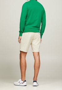 Pull vert à manches longues en tissu léger ; short beige en matériau respirant ; baskets blanches avec des accents rouges et bleu marine, design décontracté.