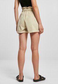 Beige shorts med høy, elastisk midje, rullet nederkant og to baklommer, laget av et mykt, lett stoff.