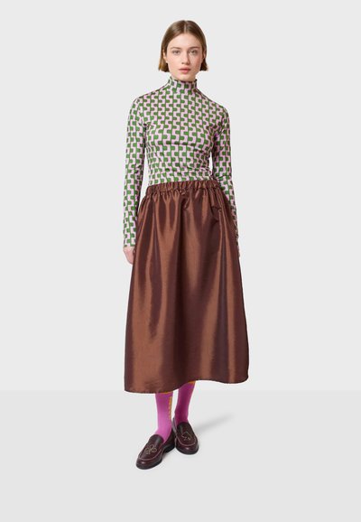 Langärmliger Rollkragenpullover im grünen und rosa geometrischen Muster, kombiniert mit einem satinbraunen Rock, abgerundet mit rosa Socken und braunen Slippern.