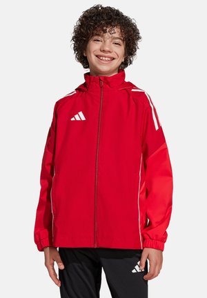 Rode jas met witte accenten en gestreept ontwerp, met een hoge kraag, ritssluiting en elastische boorden. Gemaakt boven een zwarte broek.