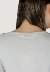 Pullover grigio chiaro con scollatura rotonda e logo LU JO scintillante impreziosito sulla schiena. Tessuto morbido e liscio.