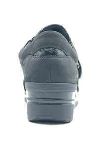 Scarpa in suede nera con un accento nero lucido, caratterizzata da una forma arrotondata, suola in gomma e tacco basso, vista dal retro.