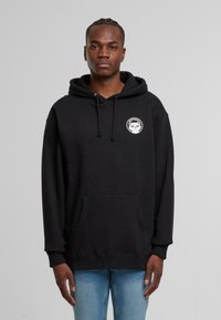 Felpa nera in cotone, con tasca a marsupio frontale e coulisse. Include una toppa rotonda con un design di gatto sul petto sinistro.