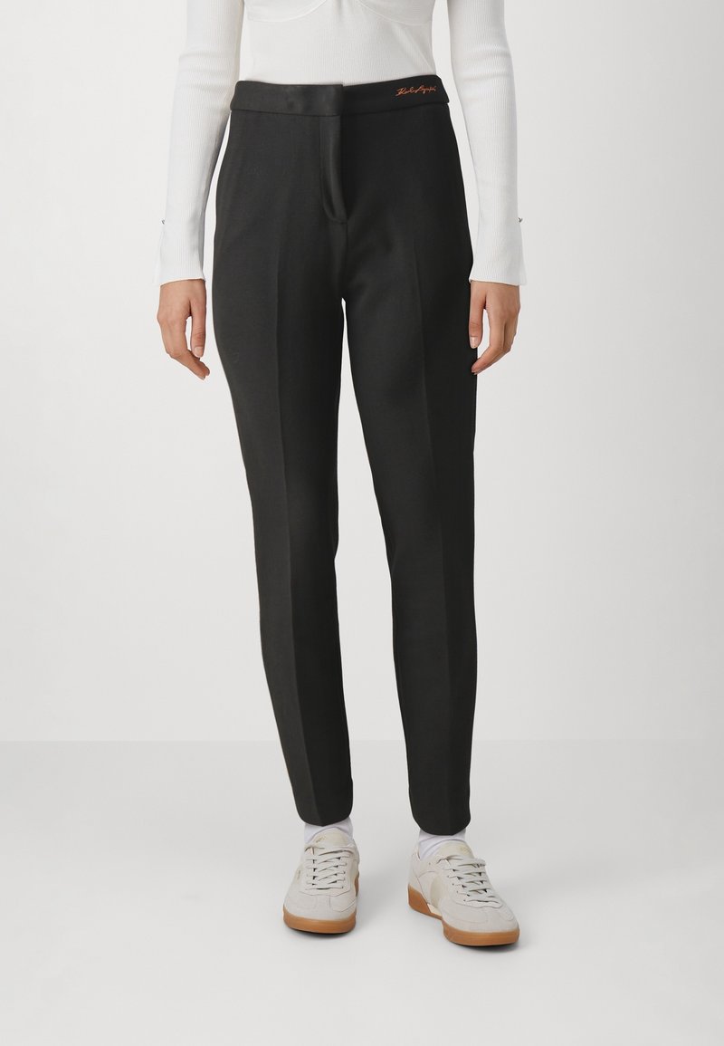 Svarta skräddarsydda byxor med en slät textur, featuring en platt midja och subtila framveck. Accenteras med orange broderi nära midjan.