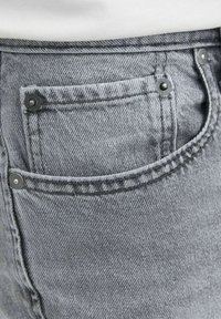 Jean en denim gris avec un design classique de poche, comportant des rivets en métal, un tissu texturé et des coutures le long des bords.