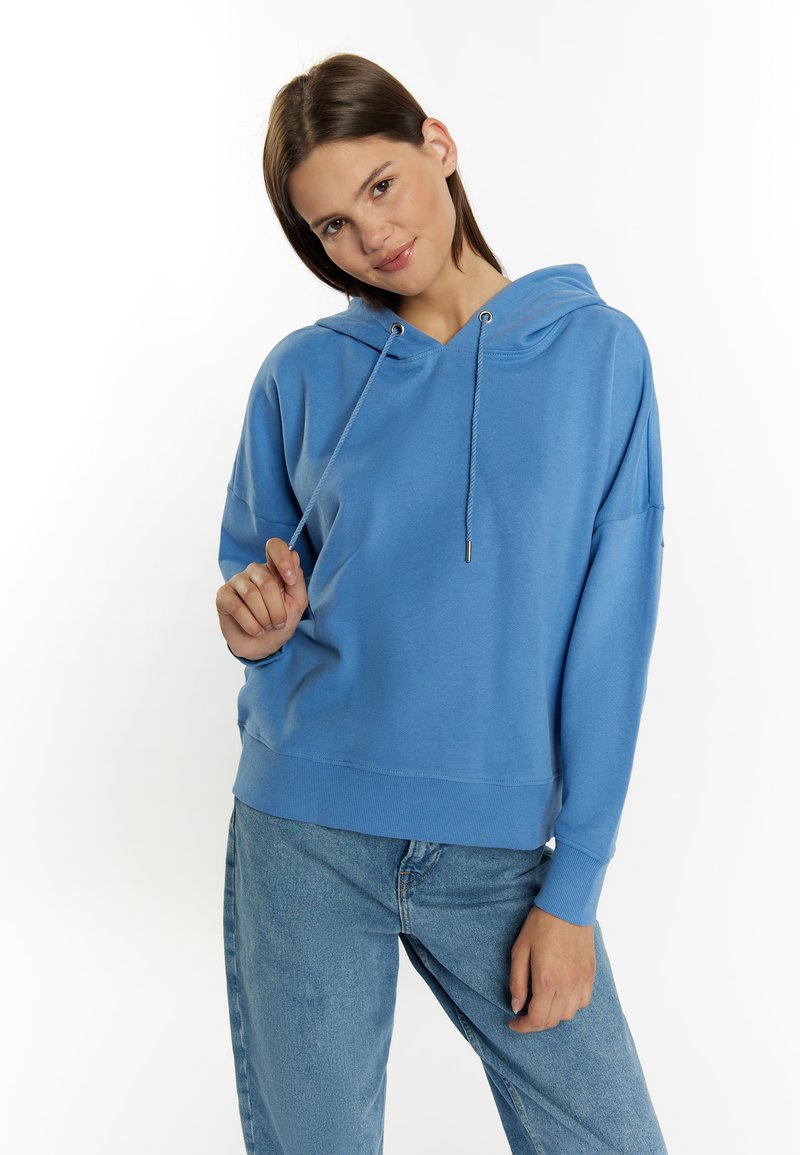 Hoodie blu realizzato in morbido tessuto, con cappuccio regolabile tramite cordino, vestibilità rilassata, polsini a coste e orlo dritto. Indossato con jeans azzurri chiari.