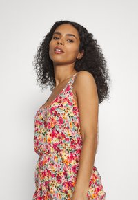 Macacão floral com um padrão multicolorido, apresentando flores rosas, laranja e amarelas sobre um fundo claro; alças finas ajustáveis.
