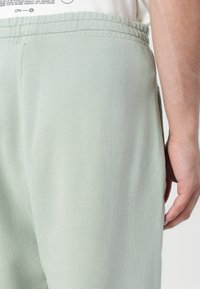 Világoszöld, puha anyagból készült jogger nadrág, rugalmas derékrésszel és oldalsó zsebekkel. Simább textúra, laza szabással.