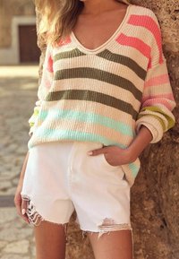 Striped knit sweater with a V-neck in soft hues of pink, olive, and blue, paired with distressed white shorts featuring frayed edges.