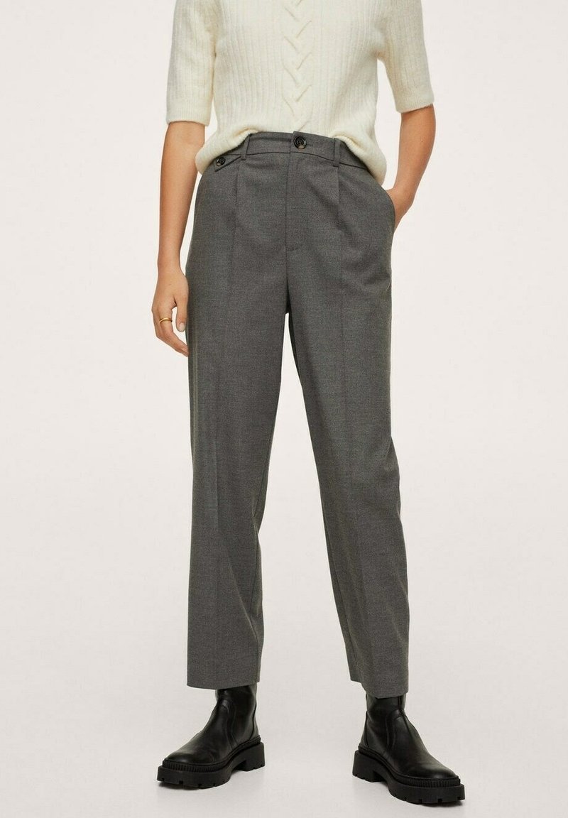 Pantalons gris sur mesure à taille haute, avec des plis avant et des poches latérales, fabriqués dans un tissu léger. Portés avec un haut en tricot crème.