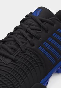 Μαύρο αθλητικό παπούτσι με υφή σχεδίου, μαύρα κορδόνια και μπλε ριγέ λεπτομέρειες στο πλάι και στη σόλα για αθλητικό στυλ.