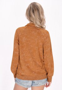 Rostfärgad pullover med en texturerad, mjuk tyg. Har en krage, raglanärmar och en ribbad nederdel. Matchas med denimshorts.