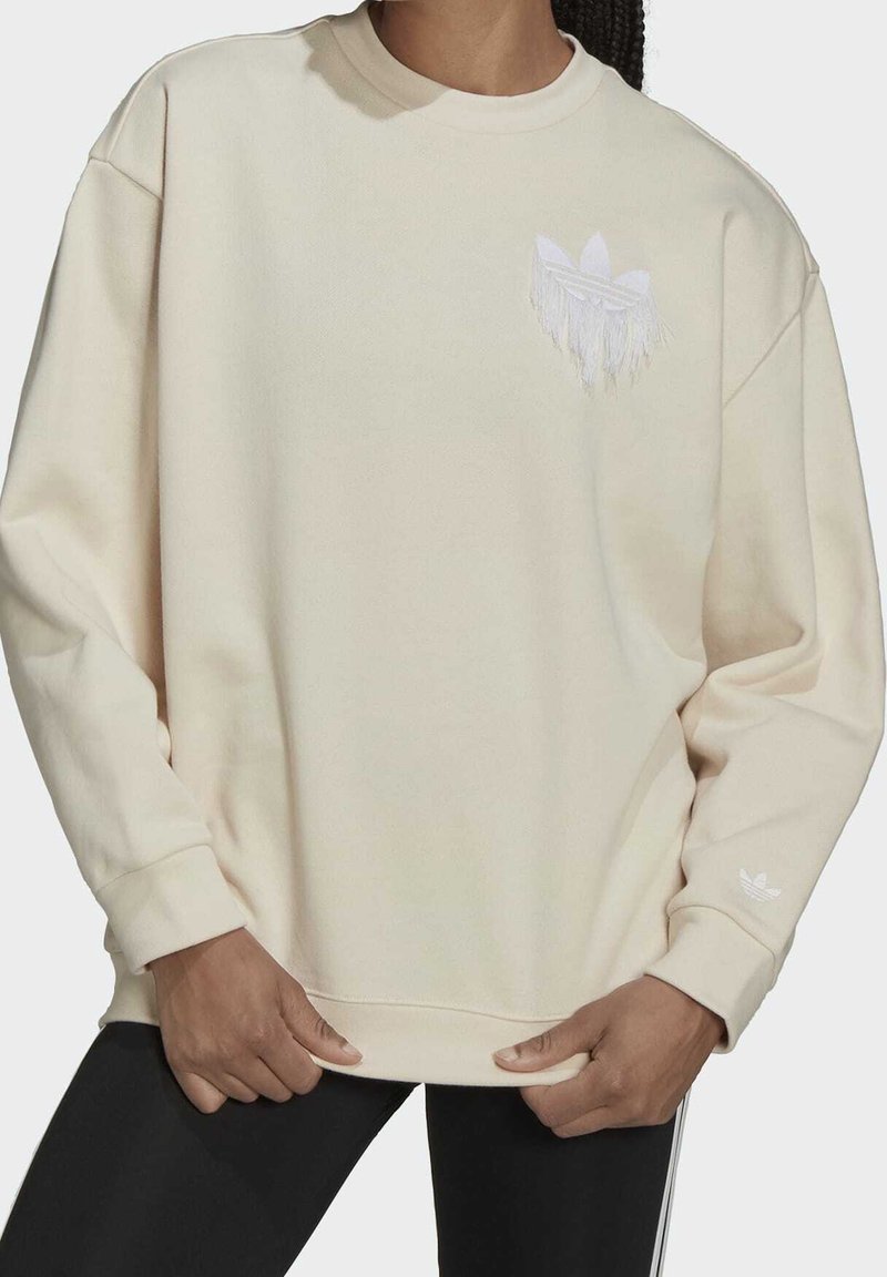 Beige oversized sweatshirt with a crew neckline, featuring a white embroidered logo and fringe detail on the chest, and ribbed cuffs.