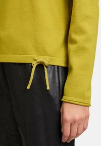 Maglione giallo con finitura testurizzata, dotato di un dettaglio con cordoncino all'orlo e polsini a coste; abbinato a pantaloni in materiale lucido neri.