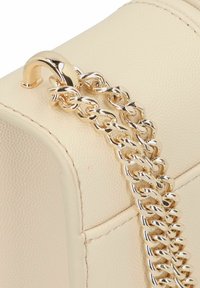 Beige Lederhandtasche mit strukturierter Oberfläche, ausgestattet mit einem vergoldeten Kettenriemen und einem glänzenden Verschlussdetail.