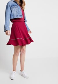 Punane kleit, millel on laienev seelikuosa, valge õmbluse detail, millele on lisatud heledat denimpusakut ja valgeid tennisetossusid, ning millel on keha lähedane varrukas.