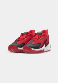Red athletic shoes with black accents, mesh panels, and white soles. Features textured laces and a logo on the tongue for branding.