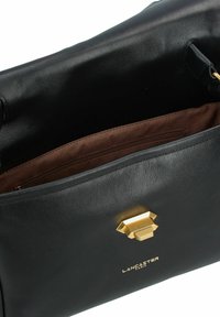 Borsa a tracolla in pelle nera con una superficie liscia, hardware geometrico dorato e un interno in tessuto marrone con tasca con cerniera. Logo del brand visibile.