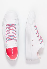 Białe płócienne trampki z różowo-niebieskimi plecionymi sznurówkami, teksturowaną gumową podeszwą i różowym wnętrzem. Posiadają logo na języku.