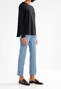 Osoba nosící černý top s dlouhým rukávem, světle modré kalhoty s ohrnutým lemem a černé lesklé mokasíny na nazouvání s přezkou.