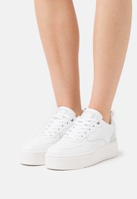 Sneaker bianchi con tomaia in pelle liscia, design con lacci e dettagli in texture a contrasto. Presentano una suola spessa e testurizzata.