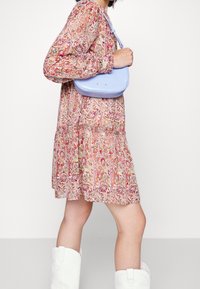Borsa a mano azzurro chiaro con una forma arrotondata, texture liscia e accessori a contrasto. Indossata con un vestito a fantasia floreale e stivali da cowboy bianchi.