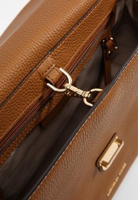 Sac à main en cuir texturé marron avec quincaillerie dorée. Il dispose d'une poche zippée et d'une doublure intérieure lisse. Design compact et structuré.