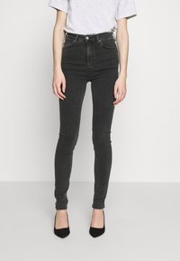 Černé skinny džíny s vysokým pasem vyrobené z denimu, s hladkou texturou, designem se pěti kapsami a mírným vyblednutím. Vyneseny s černými podpatky.