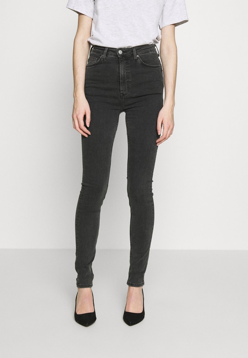 Černé skinny džíny s vysokým pasem vyrobené z denimu, s hladkou texturou, designem se pěti kapsami a mírným vyblednutím. Vyneseny s černými podpatky.