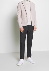 Světle růžový texturovaný blazer, bílý rolák, tmavě šedé zúžené kalhoty a bílé tenisky. Významné detaily: dvojí přední kapsy a zapínání na knoflík.
