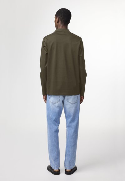 Olive green long-sleeve shirt with a straight cut, paired with light blue jeans. The outfit features simple seams and a smooth texture.