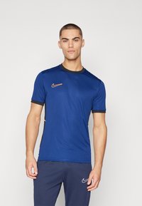 Blå treningst-skjorte med korte ermer, svarte detaljer på kragen og ermene, og en liten oransje Nike-logo på brystet.