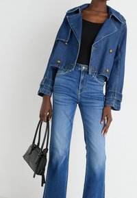 Giubbotto di jeans con grande colletto e chiusura a doppi bottoni, abbinato a jeans blu a zampa d'elefante. Borsa nera con doppi manici.