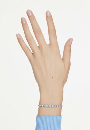 Pulsera de plata con gemas redondas de color azul claro, llevada en una mano con esmalte de uñas natural. La mano está extendida contra un fondo claro.