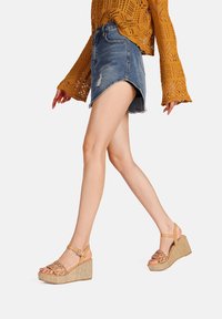 Sandali wedge beige con design a strap intrecciato, dotati di una cinghia alla caviglia e di un tacco wedge in fibra naturale testurizzata.