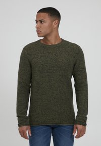 Grønn strikkegenser med rund hals og lange ermer, med et teksturert mønster. Båret sammen med blå jeans.