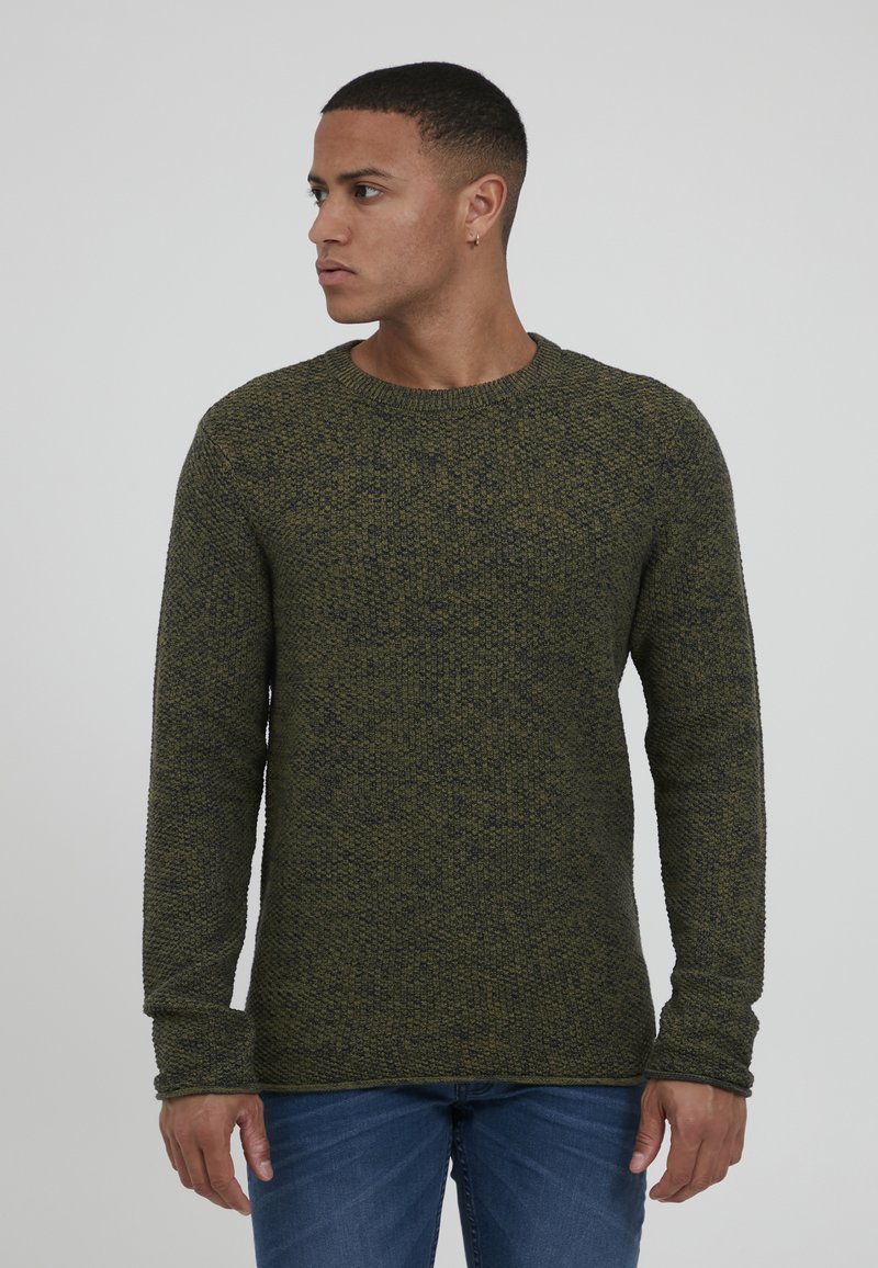 Grønn strikkegenser med rund hals og lange ermer, med et teksturert mønster. Båret sammen med blå jeans.