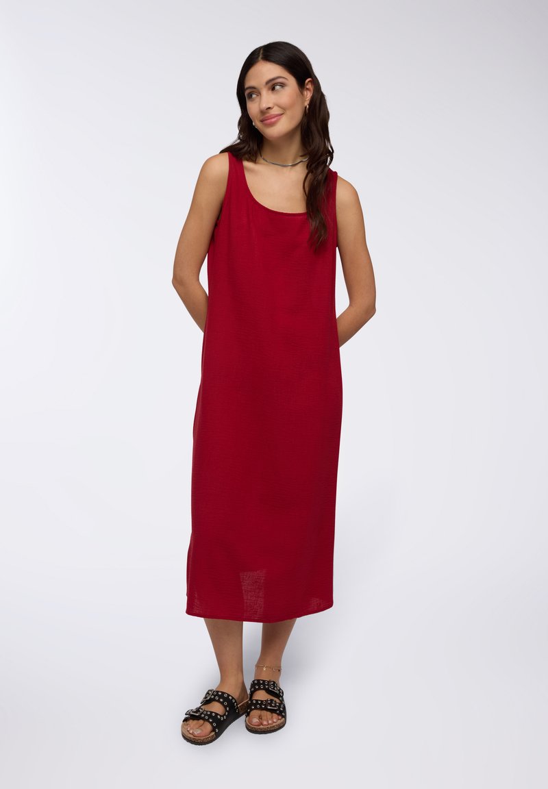 Vestito rosso senza maniche con una vestibilità rilassata, texture morbida e taglio dritto. Abbinato a sandali neri con grandi borchie.