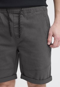 Graue Shorts aus leichtem Stoff, mit einem elastischen Bund und schwarzem Kordelzug, Seitentaschen und umgeschlagenen Säumen.